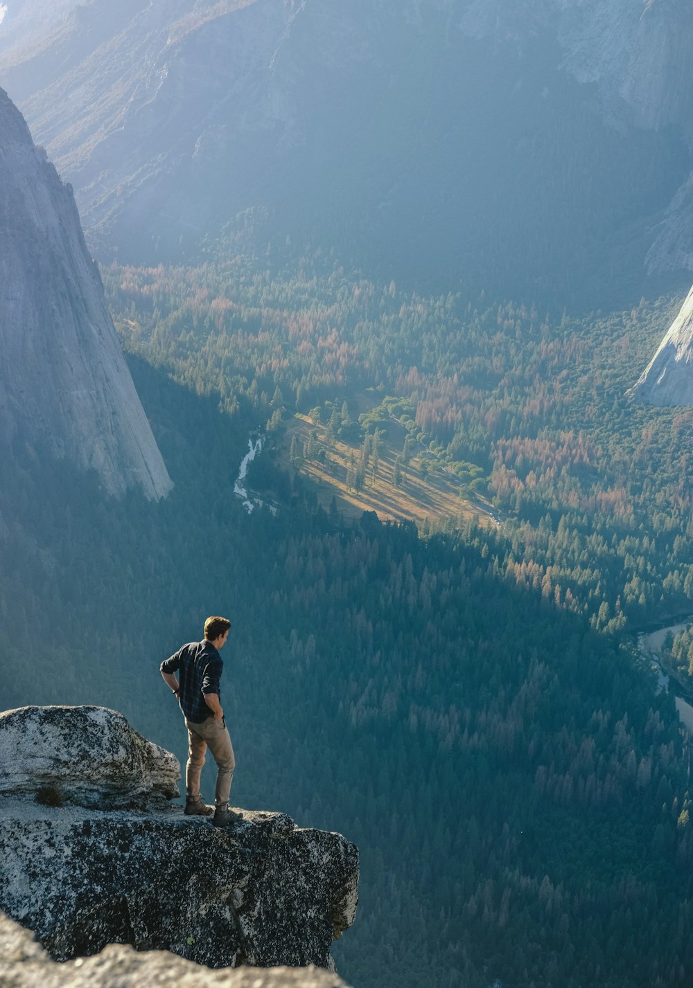 崖の上の灰色の岩の上に立っている男と昼間の森の眺め