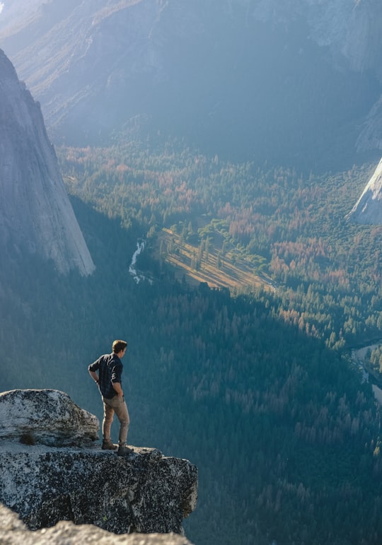 man standing on grey rock on cliff with overview of forest during daytime in Yosemite National Park United States