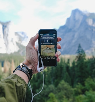 person playing music on space gray iPhone 5s with EarPods on hand during daytime