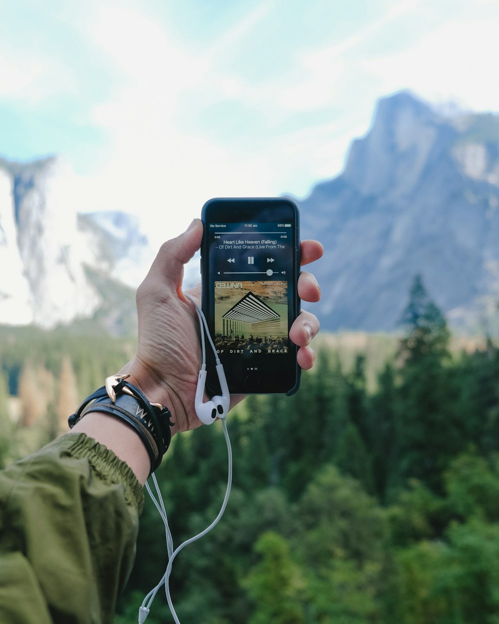A person's outstretched hand holding an iPhone with a music player in the Yosemite Valley