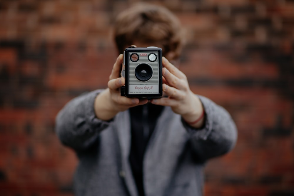 Fotografia con messa a fuoco selettiva di una persona che tiene in mano una macchina fotografica grigia e nera