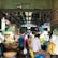 A bustling indoor market with various vendors selling a wide array of fresh produce, including vegetables and fruits. The market is crowded with people engaging in transactions and carrying bags, creating a lively atmosphere.