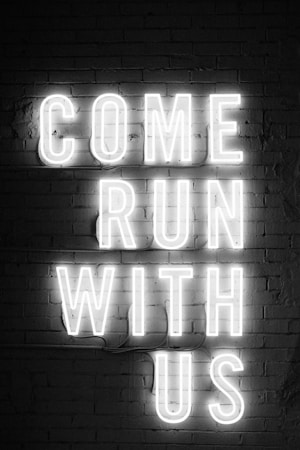 Neon lights form the words 'COME RUN WITH US' on a brick wall background in a vertical layout. The glowing letters create a striking contrast against the dark wall.