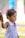 A young child wearing a colorful striped dress is holding onto an adult's hand, suggesting a sense of security. The child's expression appears contemplative as they look into the distance. The background is blurred, emphasizing the child.