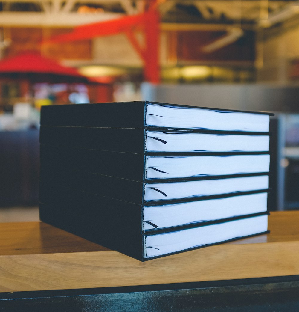 Sechs schwarze Bücher auf braunem Holztisch