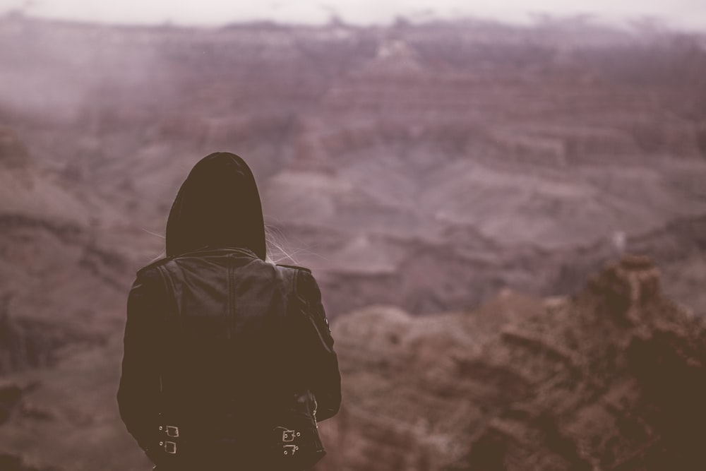 person wearing black hoodie standing at cliff