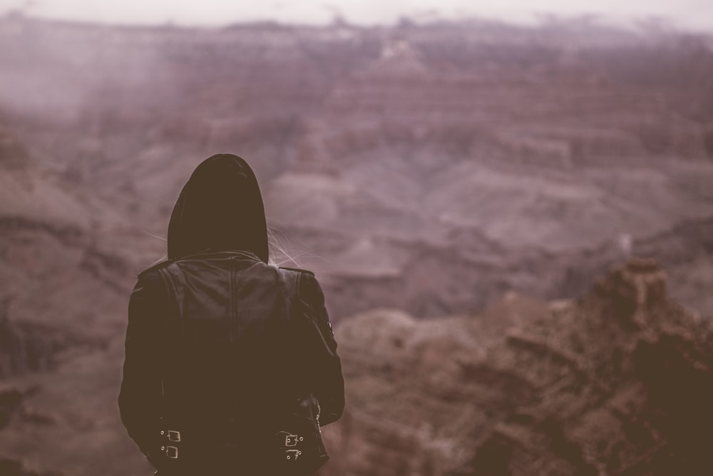 personne portant un sweat à capuche noir debout à la falaise