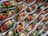 A collection of small, colorful appetizers arranged neatly in paper liners. Each piece is composed of a crispy base topped with a mixture of finely chopped herbs, diced tomatoes, and small chunks of white cheese, all garnished with leafy greens.
