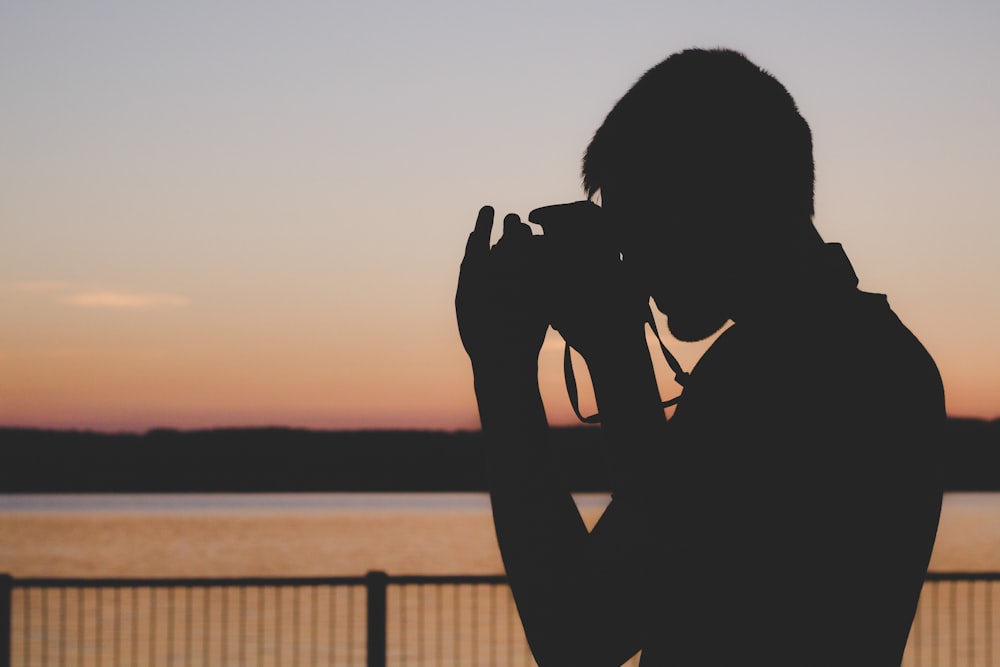 silhouette d’homme utilisant la caméra près de la balustrade pendant le coucher du soleil