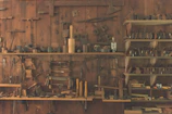 A wooden workshop wall features an array of vintage hand tools neatly organized on shelves and hanging. The tools include hammers, saws, planes, and other carpentry equipment, showcasing a rustic, historical atmosphere.