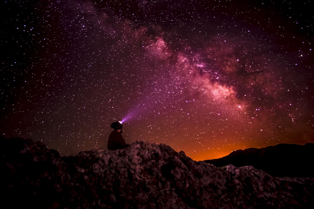 Silhouettenfoto einer Person, die eine Taschenlampe unter der Milchstraße hält