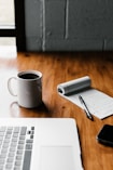 MacBook Pro, white ceramic mug,and black smartphone on table