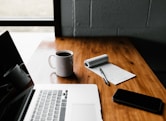 MacBook Pro, white ceramic mug,and black smartphone on table