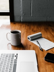 MacBook Pro, white ceramic mug,and black smartphone on table