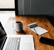 MacBook Pro, white ceramic mug,and black smartphone on table