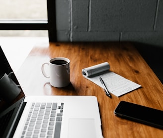 MacBook Pro, white ceramic mug,and black smartphone on table