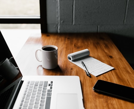 MacBook Pro, white ceramic mug,and black smartphone on table