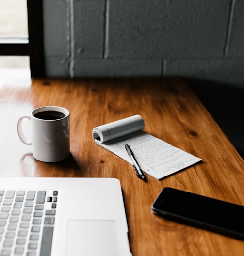 MacBook Pro, white ceramic mug,and black smartphone on table