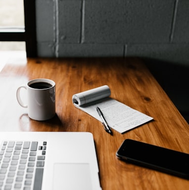 MacBook Pro, white ceramic mug,and black smartphone on table