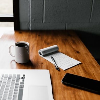 MacBook Pro, white ceramic mug,and black smartphone on table