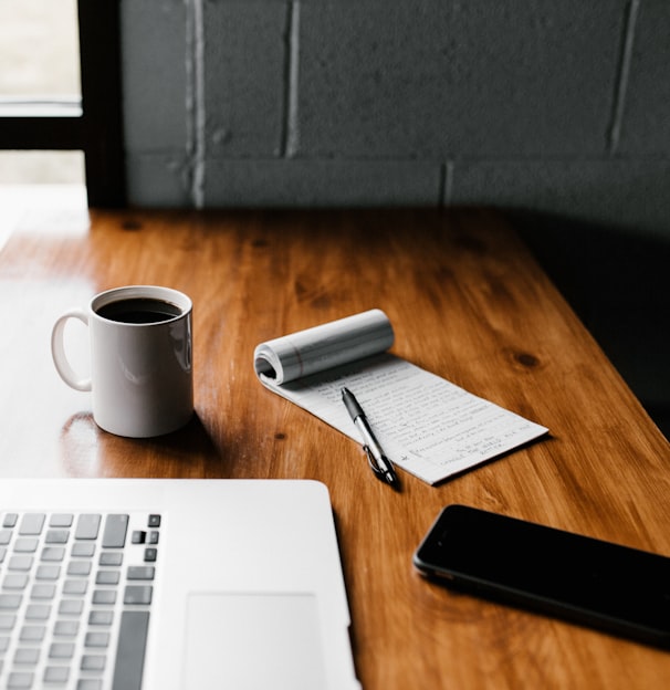 MacBook Pro, white ceramic mug,and black smartphone on table