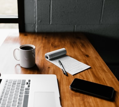 MacBook Pro, white ceramic mug,and black smartphone on table