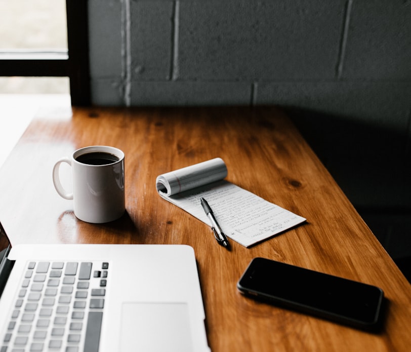 MacBook Pro, white ceramic mug,and black smartphone on table