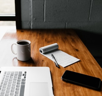 MacBook Pro, white ceramic mug,and black smartphone on table