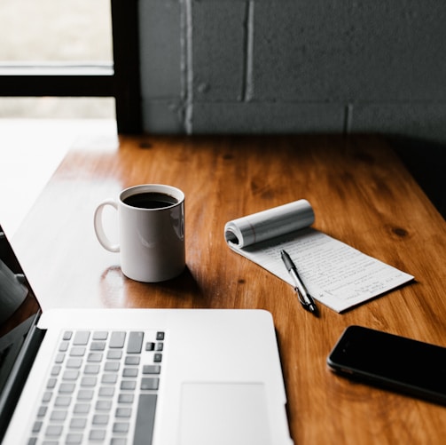 MacBook Pro, white ceramic mug,and black smartphone on table