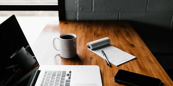 MacBook Pro, white ceramic mug,and black smartphone on table