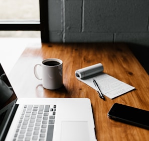 MacBook Pro, white ceramic mug,and black smartphone on table