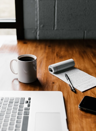 MacBook Pro, white ceramic mug,and black smartphone on table