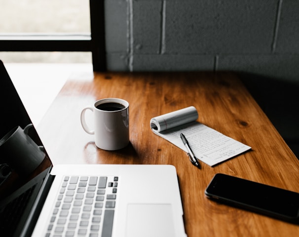 MacBook Pro, white ceramic mug,and black smartphone on table