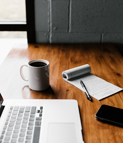 MacBook Pro, white ceramic mug,and black smartphone on table