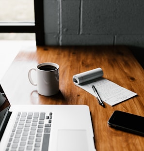 MacBook Pro, white ceramic mug,and black smartphone on table