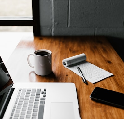 MacBook Pro, white ceramic mug,and black smartphone on table