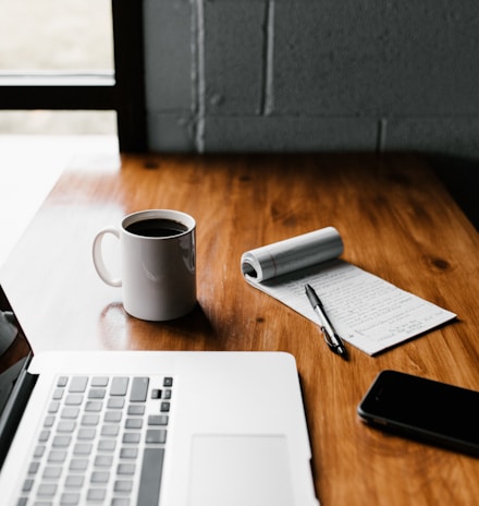 MacBook Pro, white ceramic mug,and black smartphone on table