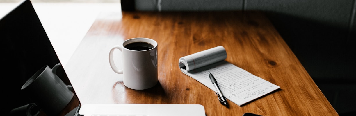 MacBook Pro, white ceramic mug,and black smartphone on table