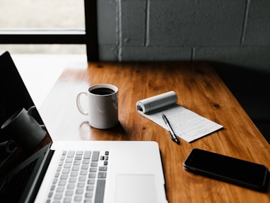 MacBook Pro, white ceramic mug,and black smartphone on table