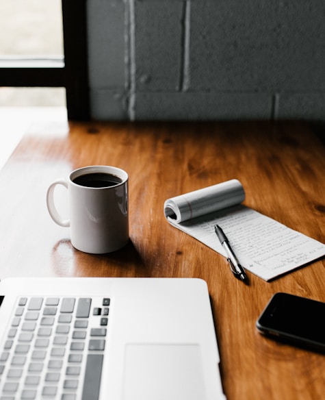 MacBook Pro, white ceramic mug,and black smartphone on table