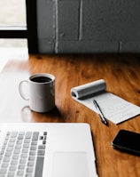 MacBook Pro, white ceramic mug,and black smartphone on table