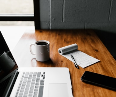 MacBook Pro, white ceramic mug,and black smartphone on table