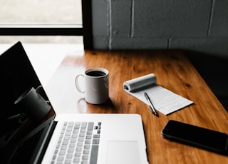 MacBook Pro, white ceramic mug,and black smartphone on table