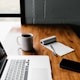 MacBook Pro, white ceramic mug,and black smartphone on table