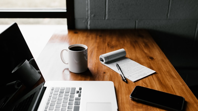Laptop on a wooden desk with coffee and notebook