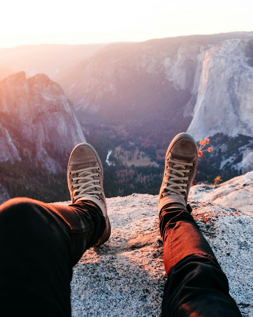 person wearing brown lace-up sneakers sitting on rocky mountain during daytime