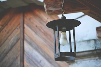 Rustic scene of an old lantern hanging from a weathered beam against a dark, textured backdrop.