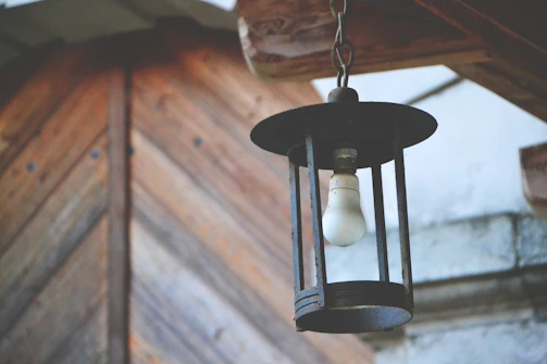 Rustic scene of an old lantern hanging from a weathered beam against a dark, textured backdrop.