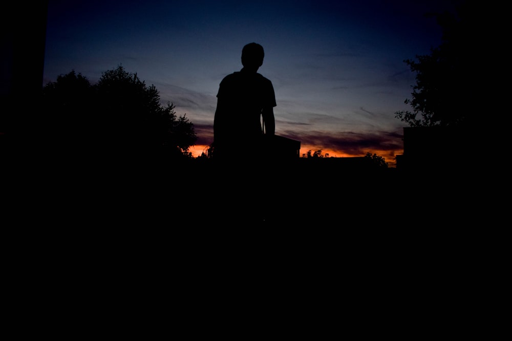 Silhouette einer Person, die während des Sunets unter blauem Himmel steht