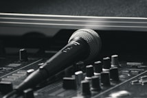A black and silver microphone resting on a sound mixing console. The image emphasizes the equipment's details, with various knobs and sliders visible in the foreground. The scene has a professional studio vibe, suggesting a focus on audio production.